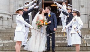 A bride and groom kissing while being surrounded by midshipmen
